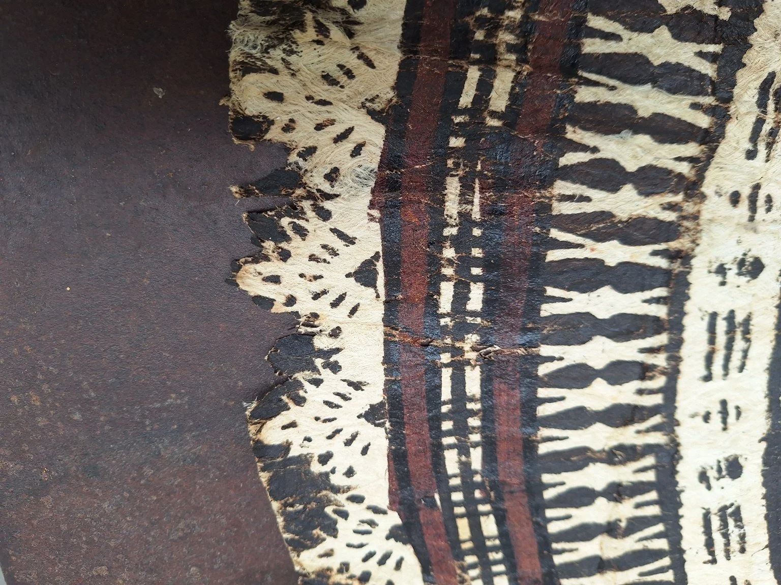 Close view of the tapa border showing layered geometric patterns, frayed fibres and small splits along the edge.