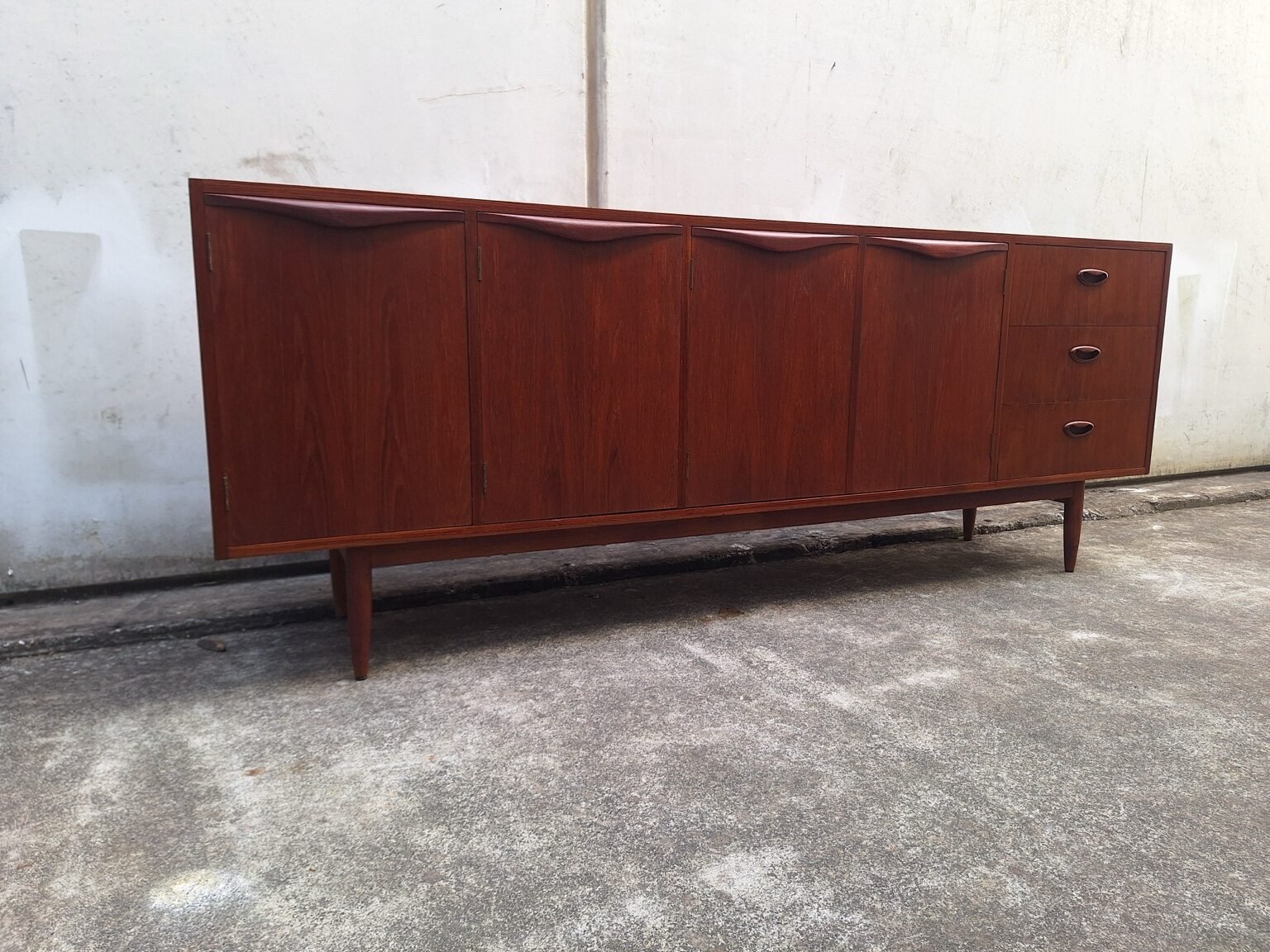 Front view of the restored Chiswell teak sideboard with four sculpted wave-handle doors, three drawers and tapered legs.