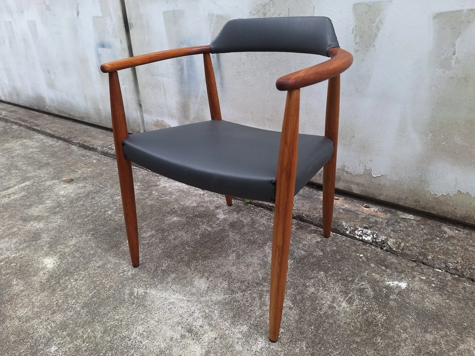 Mid-century armchair viewed from the front at an angle, showing curved timber arms and dark upholstery.