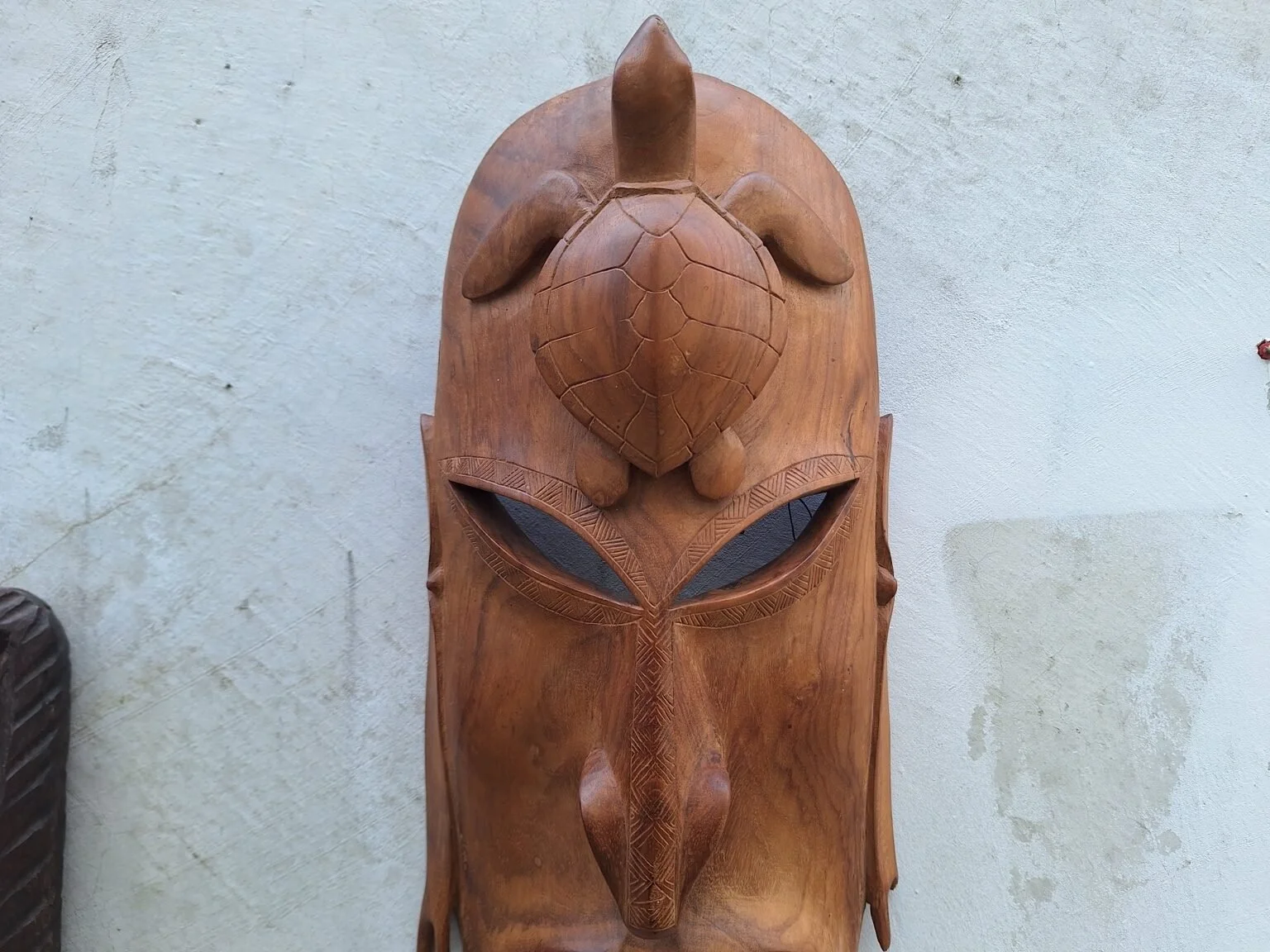 Close detail of the turtle carving and incised decoration on the lighter timber wall mask.