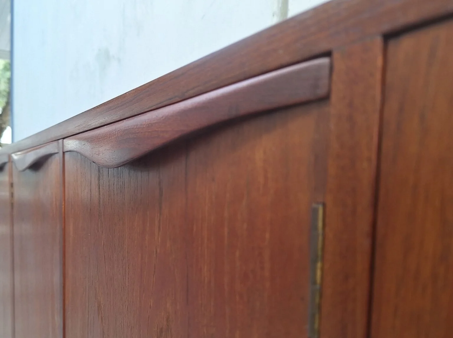 Close view of a sculpted wave handle on the teak Chiswell sideboard.