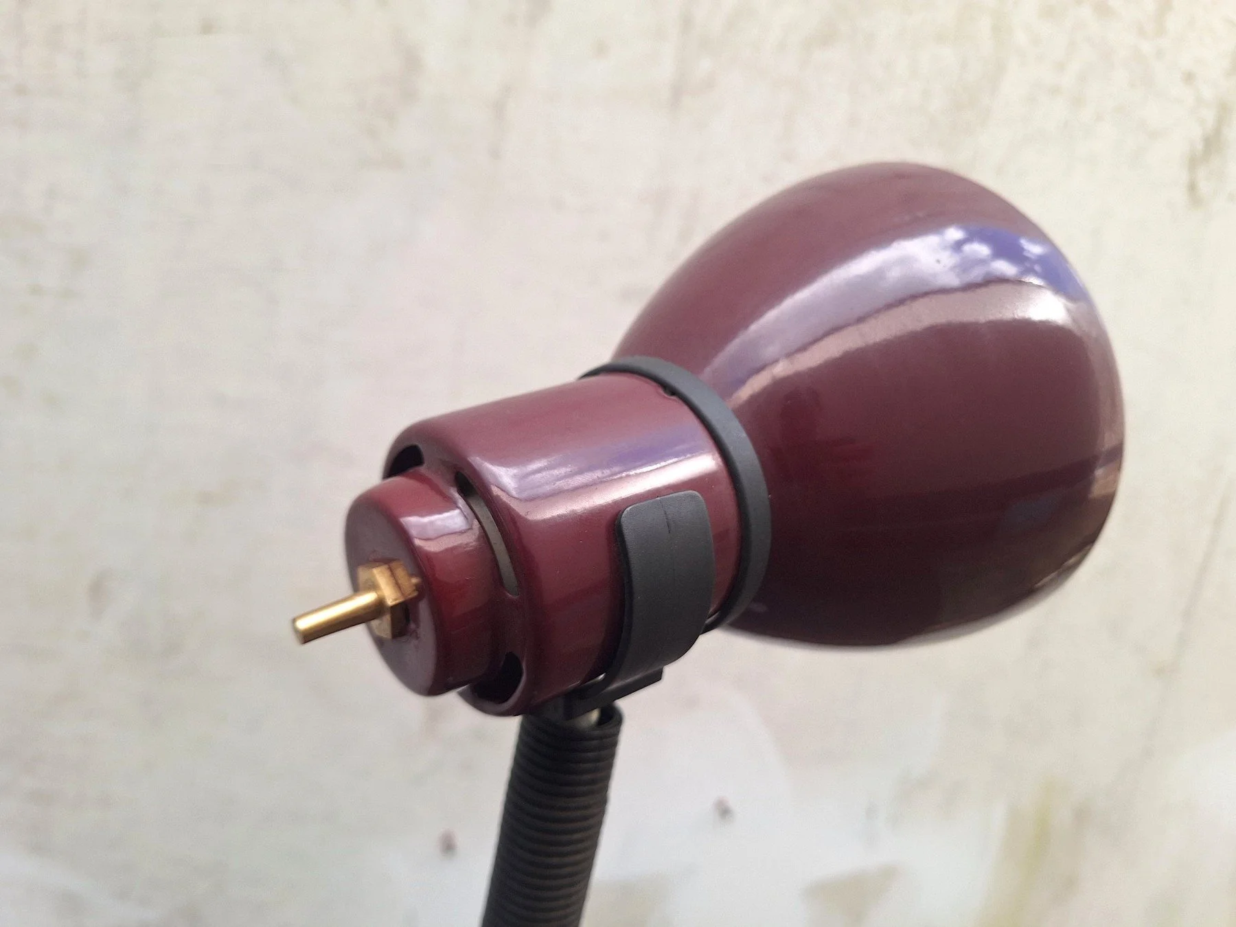 Vintage 1980s burgundy painted steel desk lamp with an adjustable gooseneck and directional shade photographed against a neutral concrete backdrop.