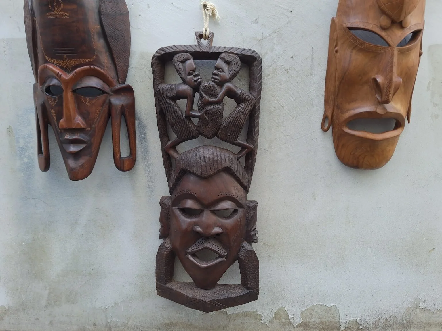 Front view of the dark carved timber figural wall panel with a central face and two figures above.