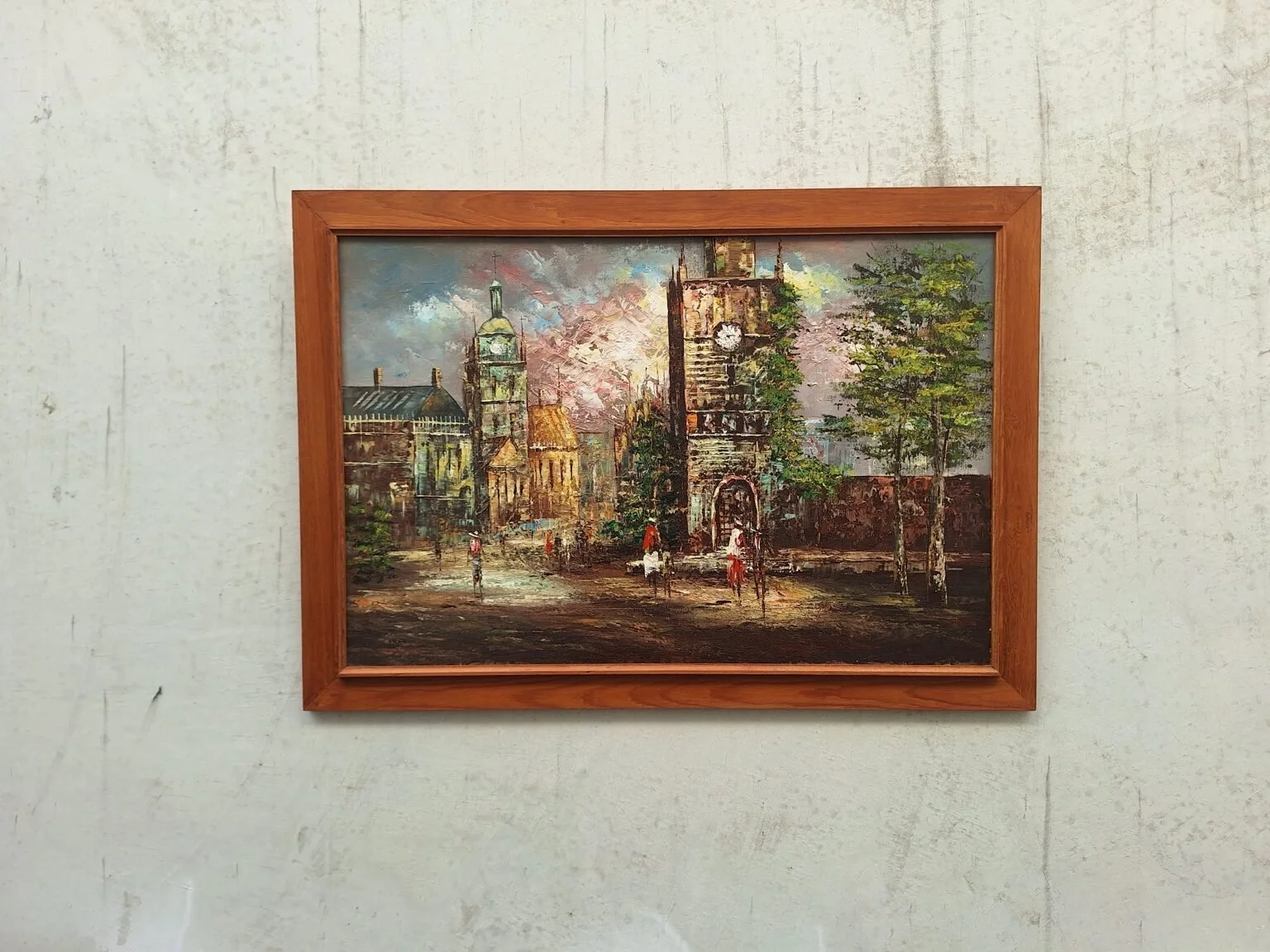 Full framed view of the vintage street scene oil painting displayed against a pale concrete wall.