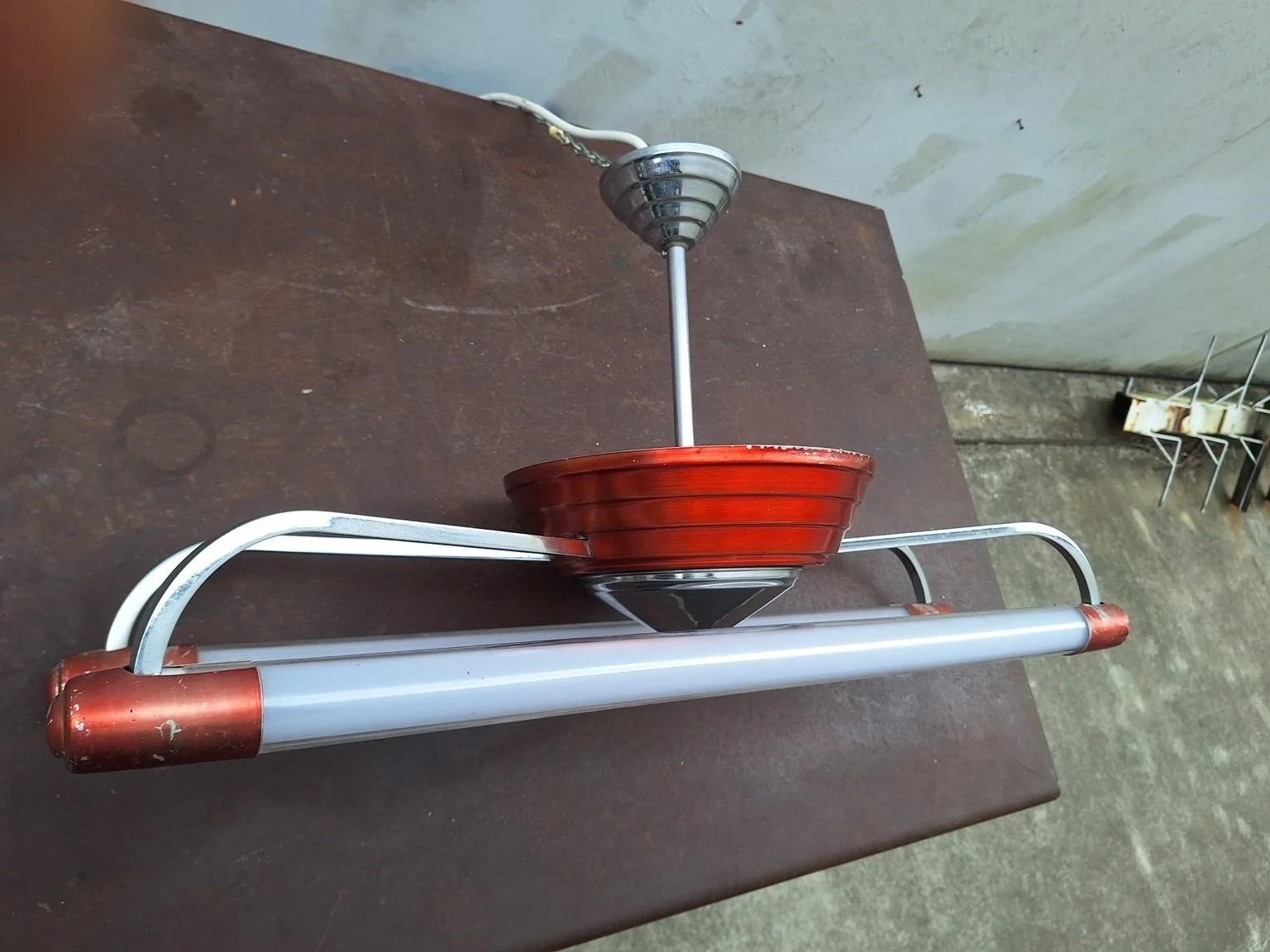 Red and chrome ceiling light laid on a table, showing its suspension stem and ceiling canopy.