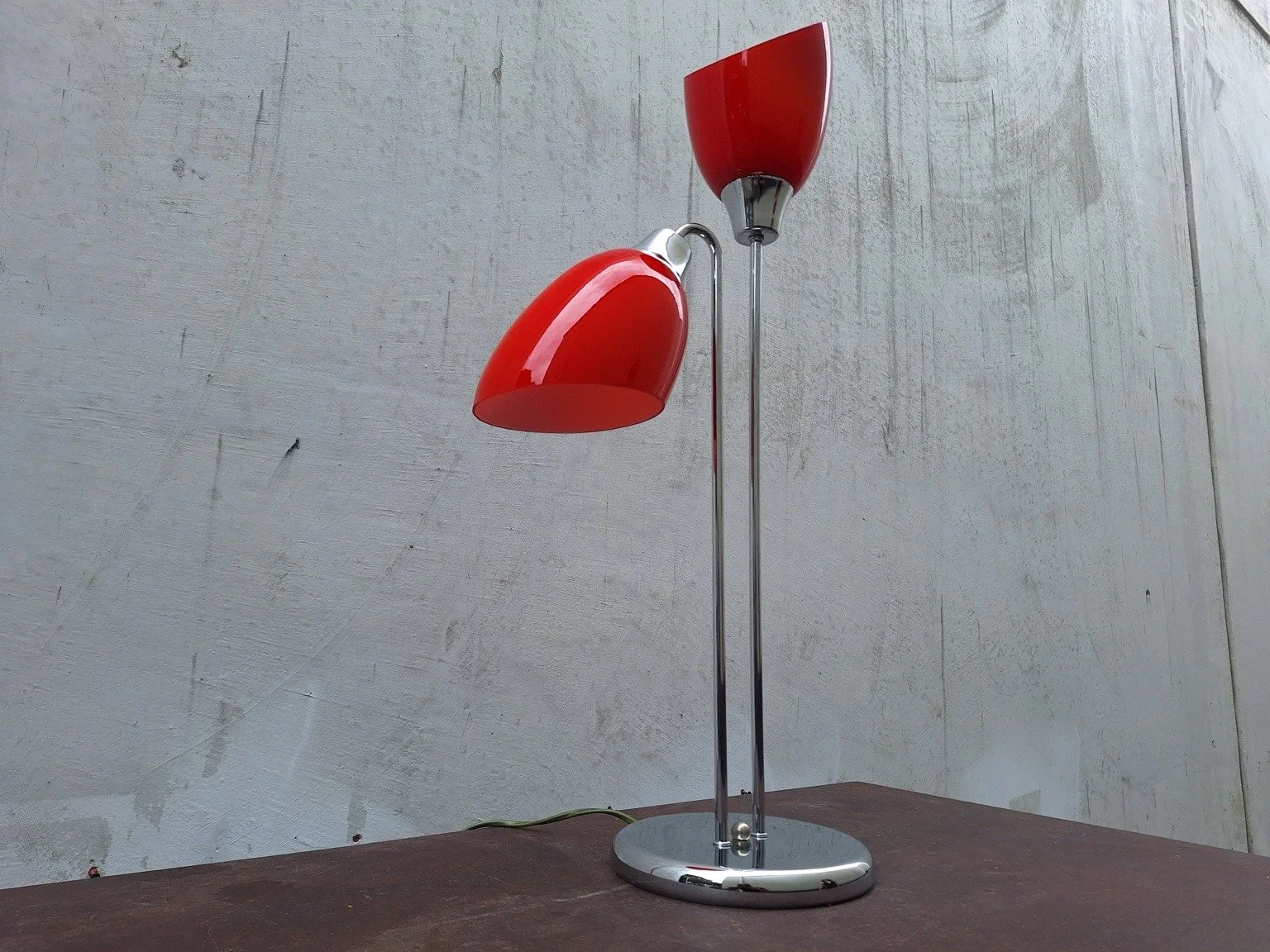 Three-quarter view of the red lamp showing its two angled shades and curved lower stem.