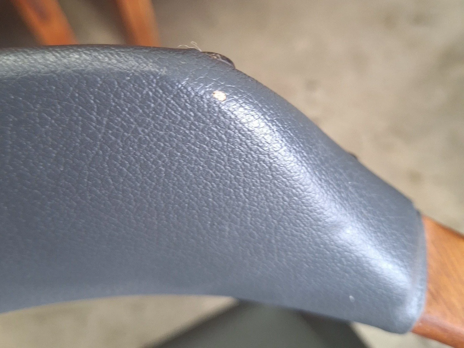 Close-up of wear and a small tear along the upholstered backrest edge.