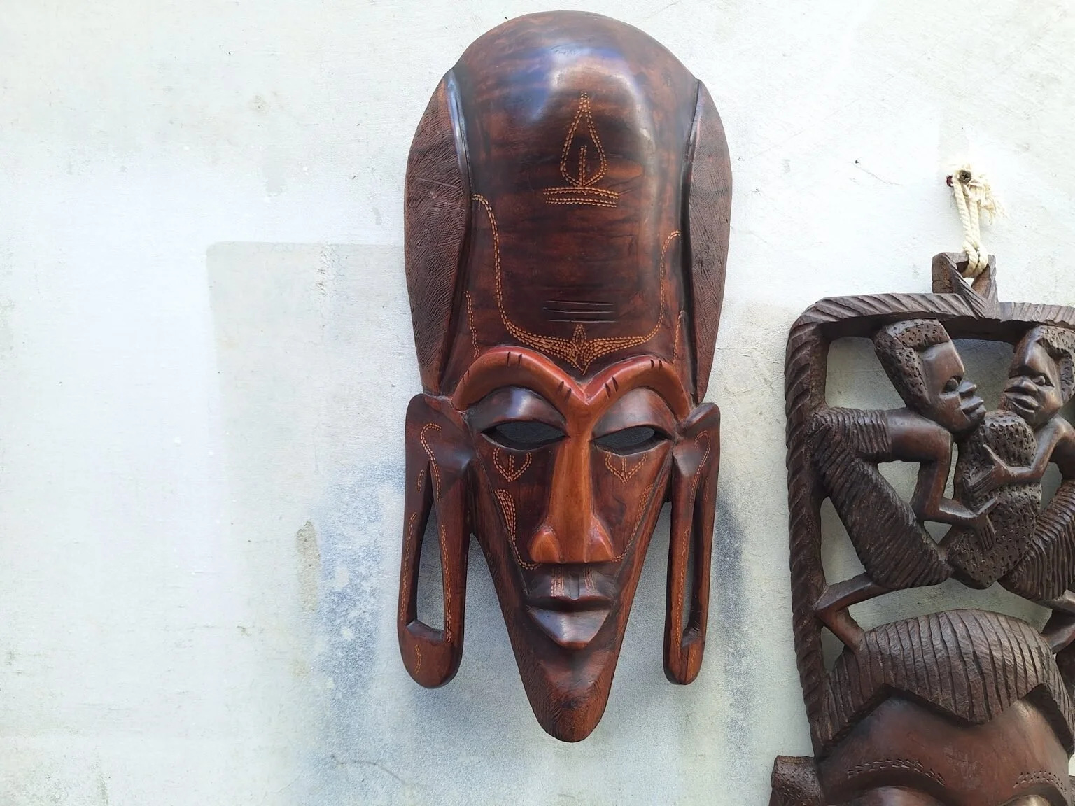 Front view of the elongated dark timber wall mask with carved facial details and long side forms.