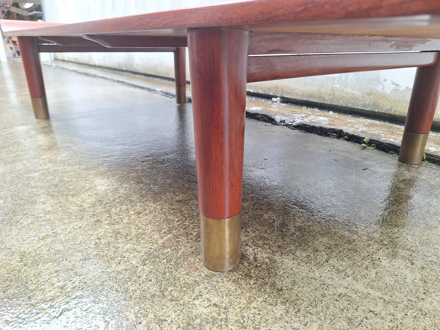 Cylindrical timber legs with brass feet and the supporting frame beneath the tabletop.