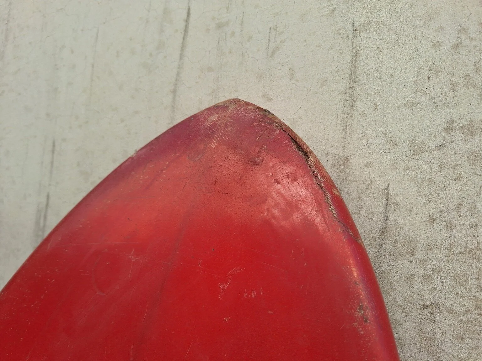 Close view of wear and surface losses around the red nose of the vintage surfboard.