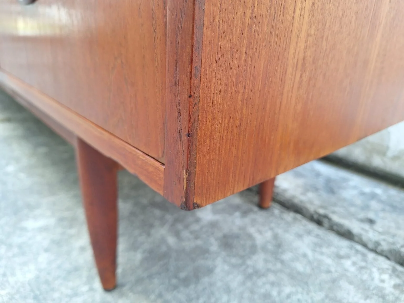 Condition detail showing a minor repaired area at the front corner of the teak sideboard.