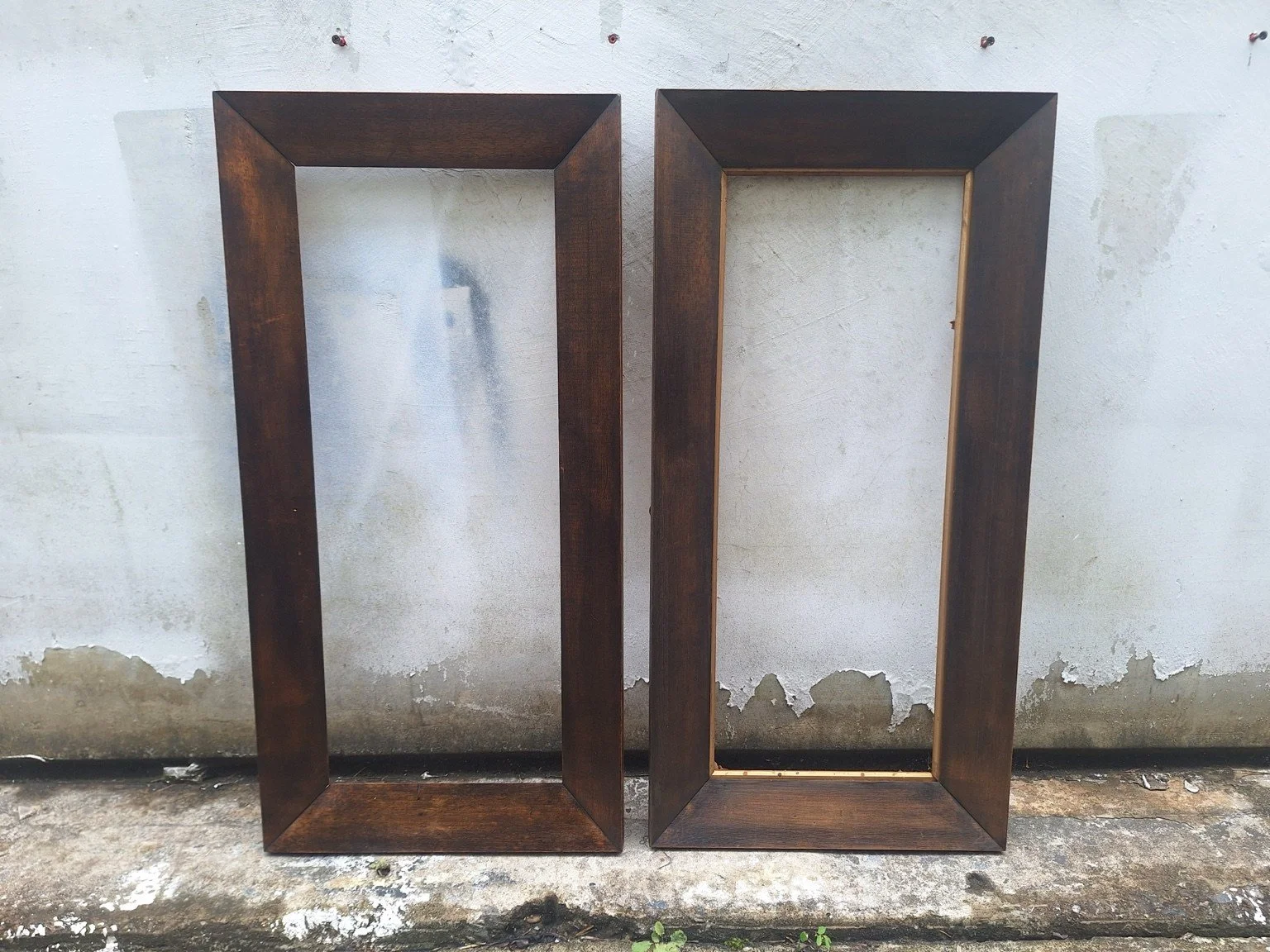 Front view of two empty vintage timber frames, one retaining a narrow gold-coloured inner slip.