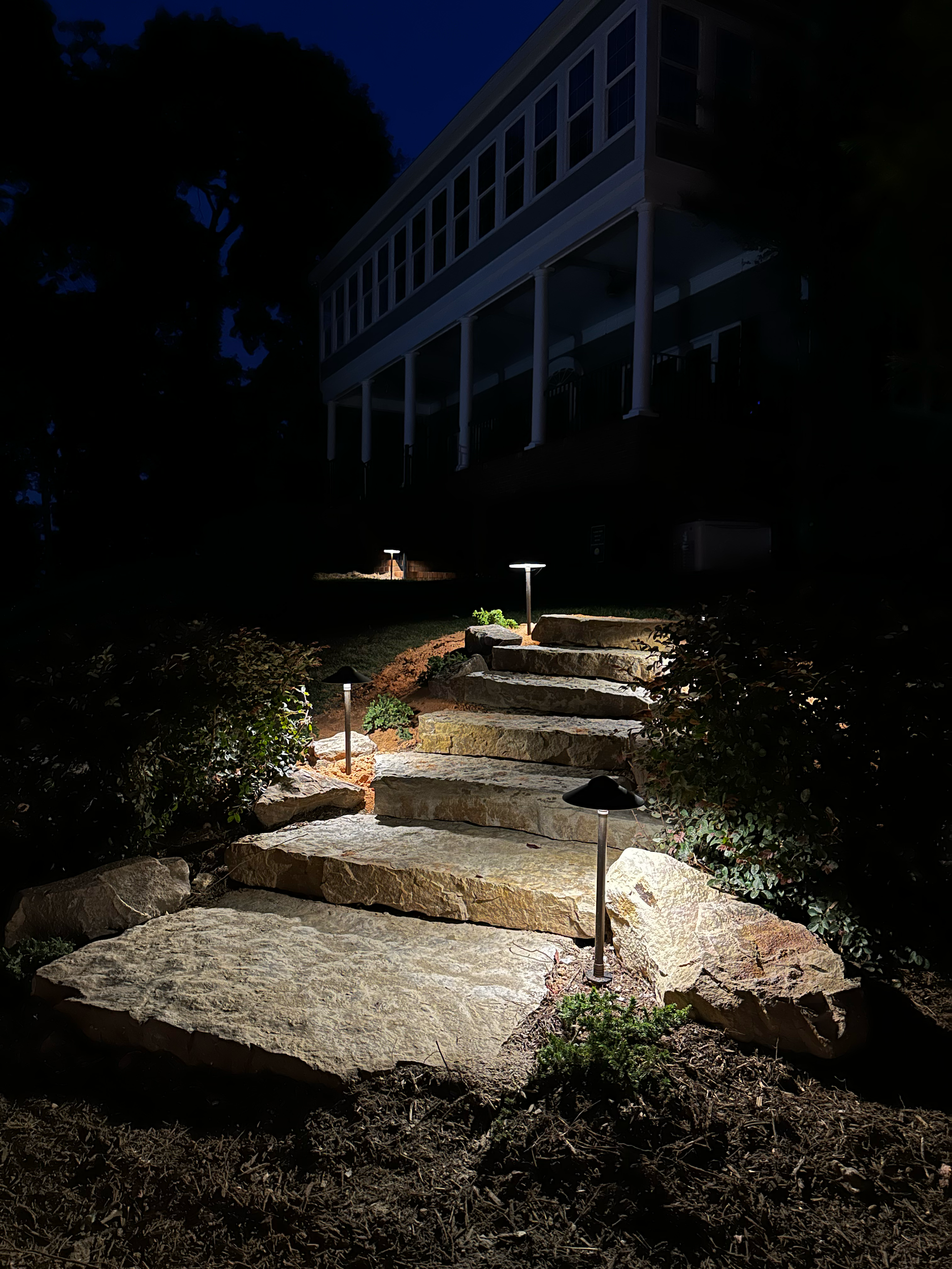 Stone pathway illuminated by small outdoor lights leading up to a house at night.