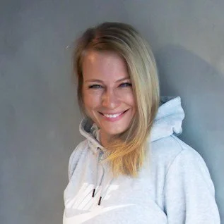 Smiling woman with blonde hair wearing a light gray hoodie against a plain background.