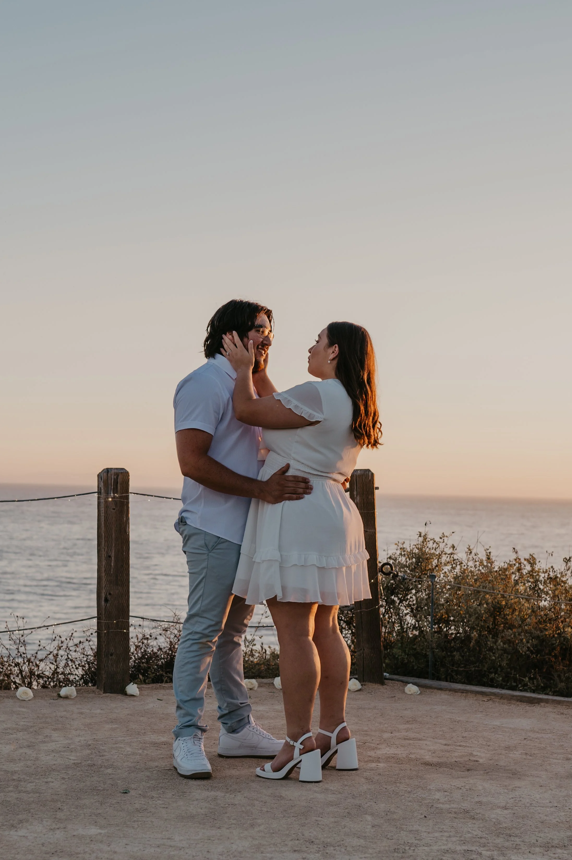 A newly engaged couple embracing with joy after the proposal, as the ocean and sunset glow create a romantic backdrop at Crystal Cove.