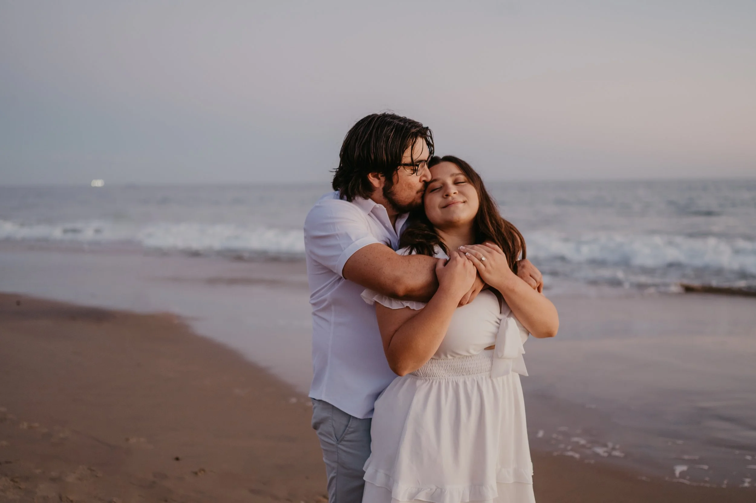 Silhouette of a couple sharing a kiss as the sun sets over the Pacific Ocean, with warm light reflecting on the water.