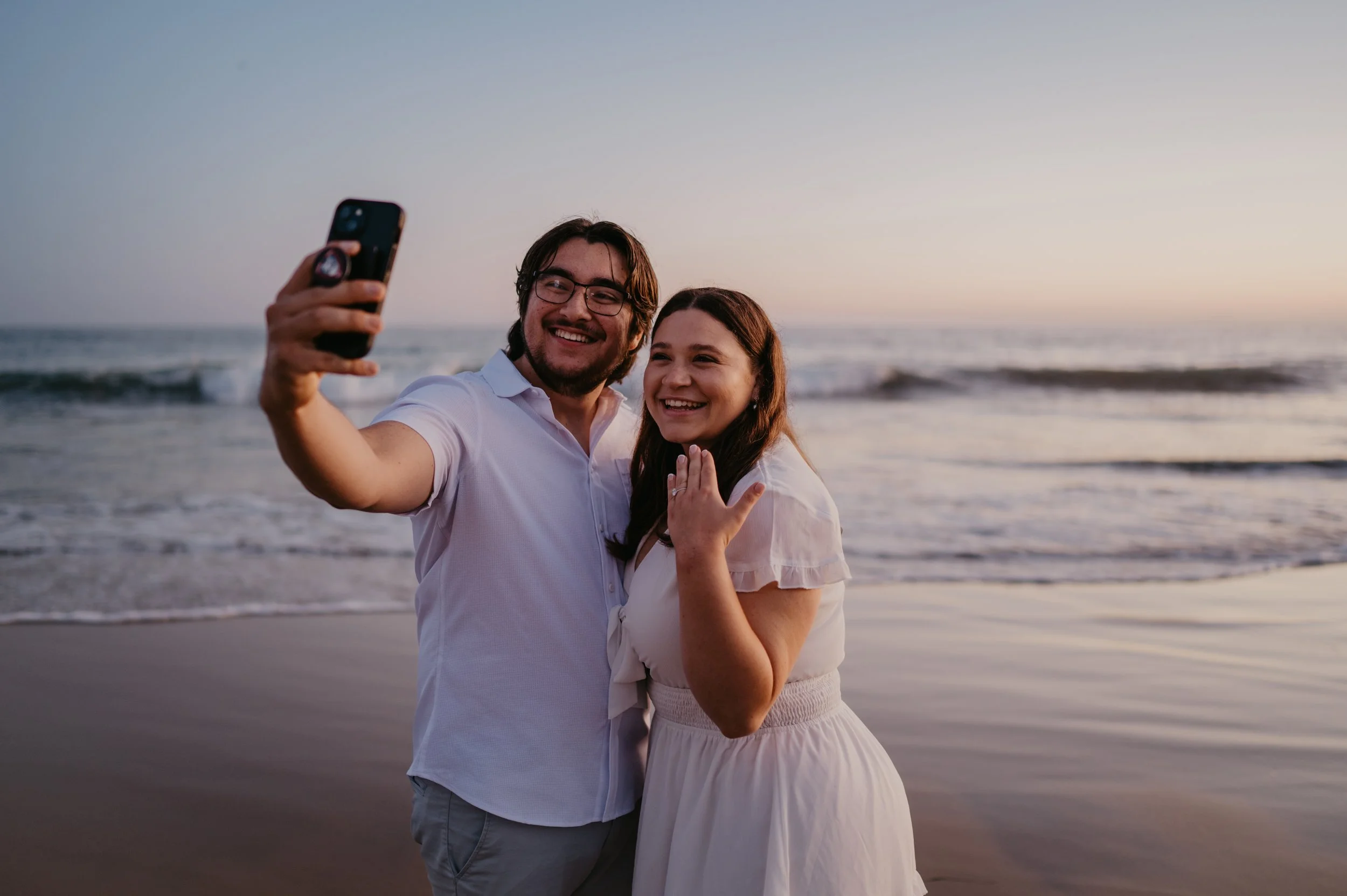 A candid moment of laughter shared between the couple on the sandy beach, with gentle waves crashing behind them at Crystal Cove State Park.