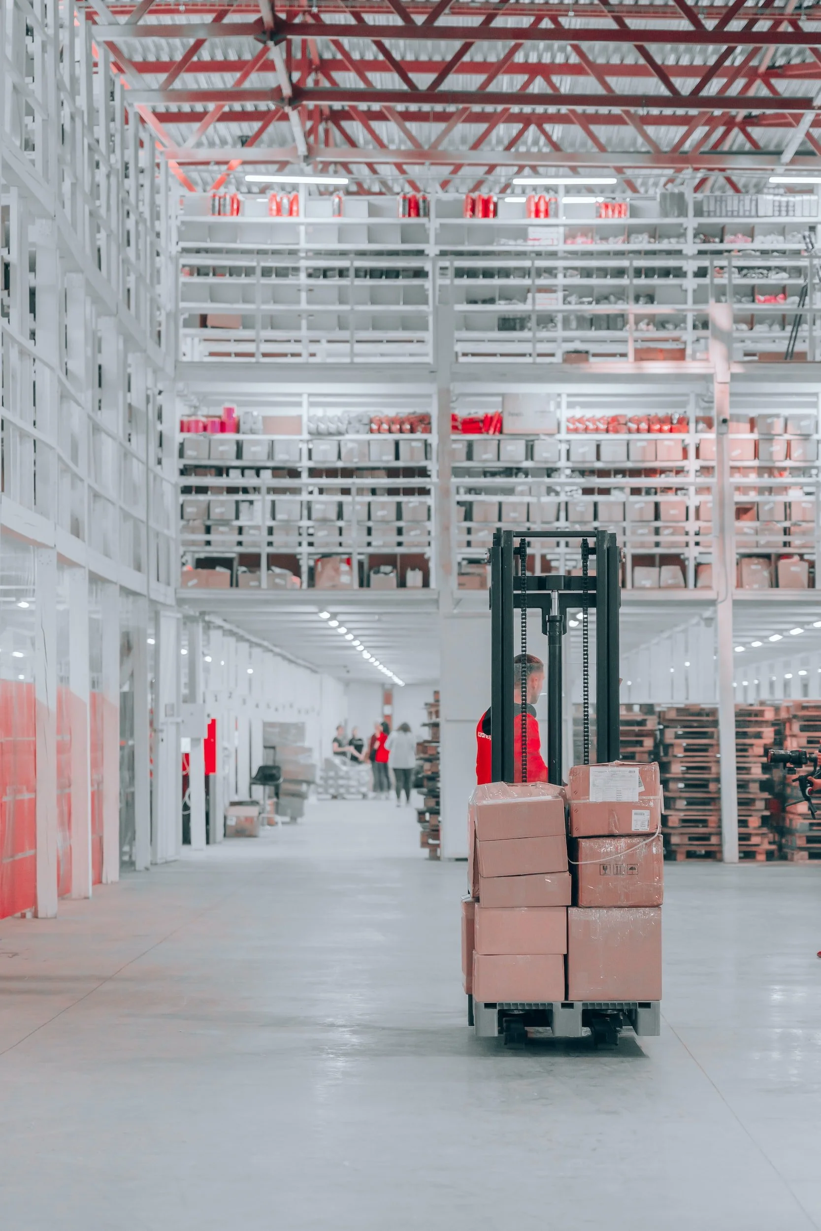 A worker operating a pallet jack inside a large warehouse storage area, surrounded by shelves stocked with boxes and packages.
