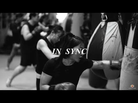 Women practicing boxing with heavy bags in a gym.