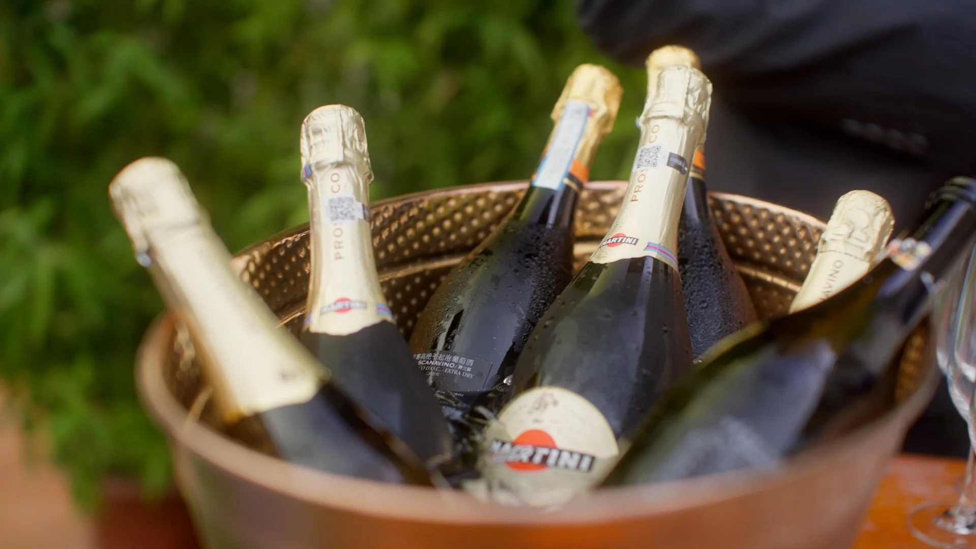 A basket of champagne bottles with condensation, placed outdoors on grass.