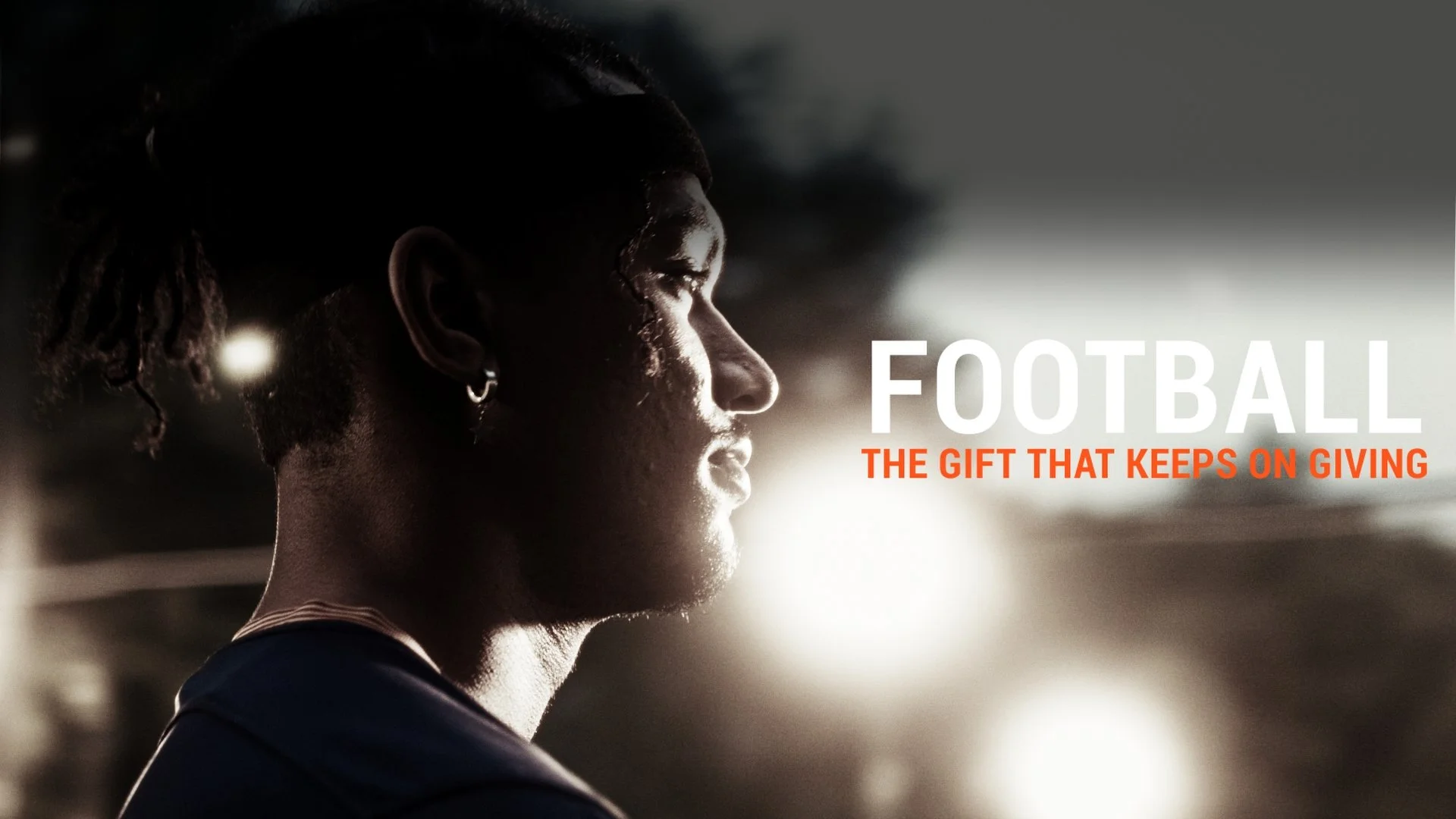 Profile of a person with dreadlocks, earrings, looking to the right in low light with the sun setting in the background. Text reads 'FOOTBALL: THE GIFT THAT KEeps ON GIVING'.