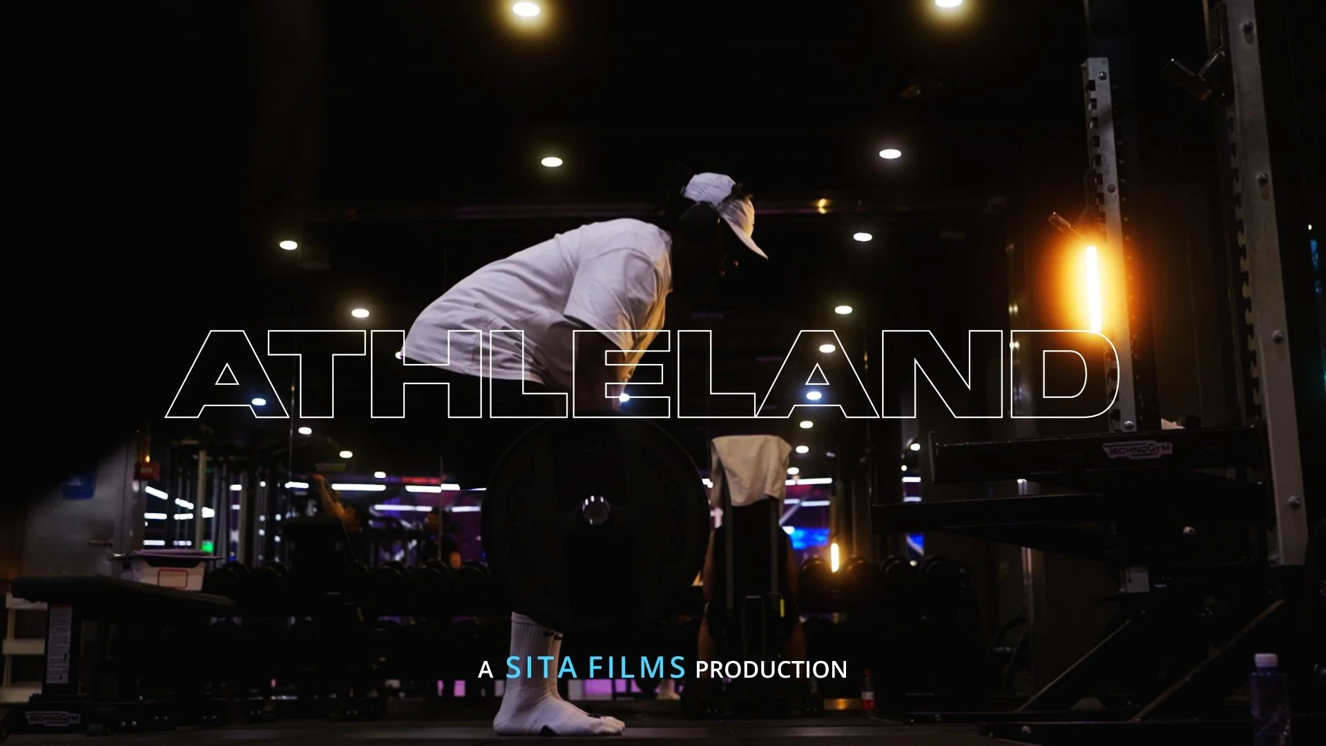 A person wearing a white shirt, shorts, and a white cap is lifting a barbell with weights in a gym. The gym has a dark environment with ceiling lights and the word 'ATHLELAND' overlaid on the image. The background shows various gym equipment and peop