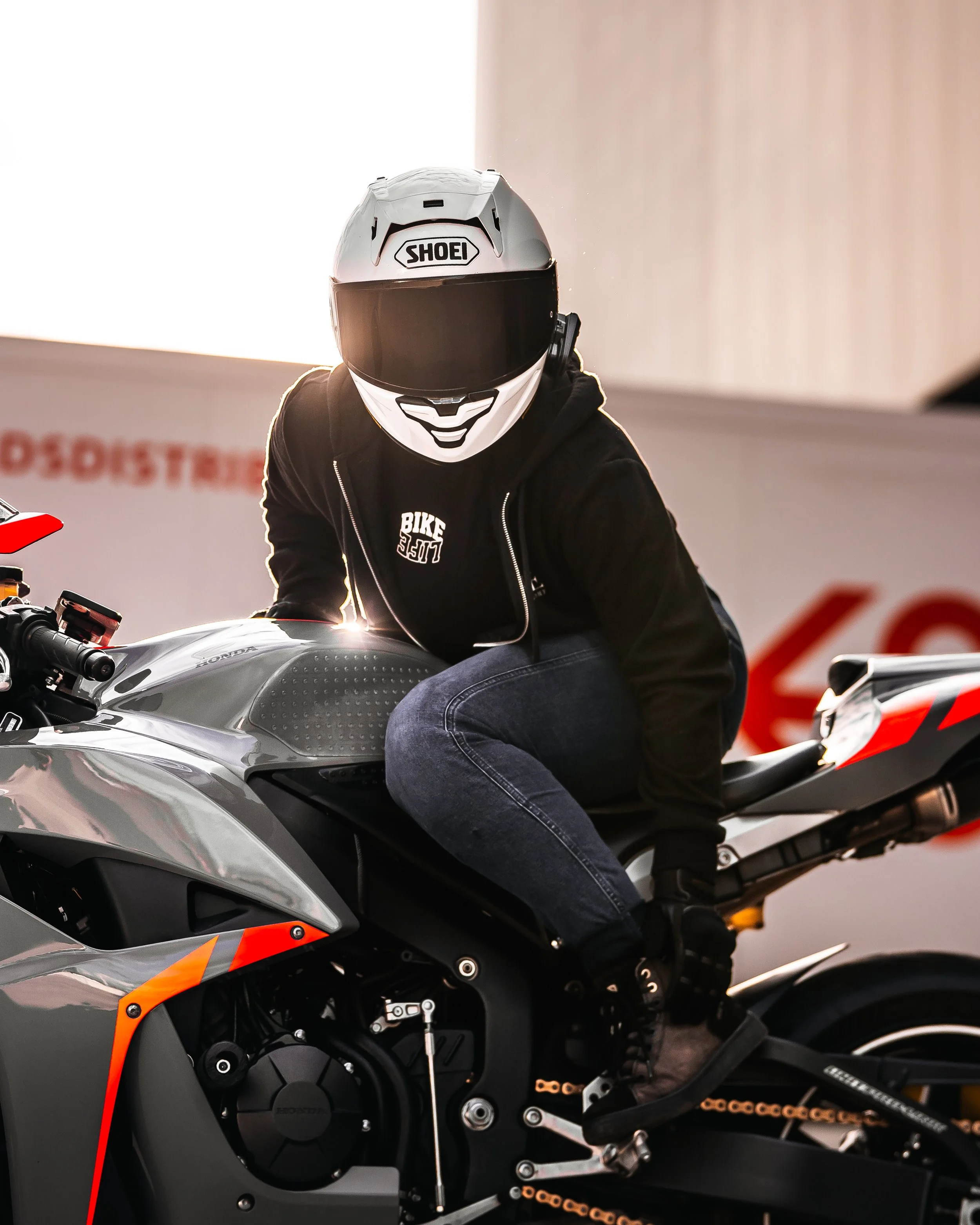 Persoon op een sportmotor met een helmpje, zittend en klaar om te rijden, in een indoor omgeving.