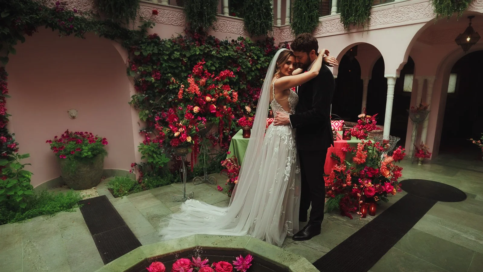 A couple share their first dance in a brightly decorated courtyard with bright pink styling.