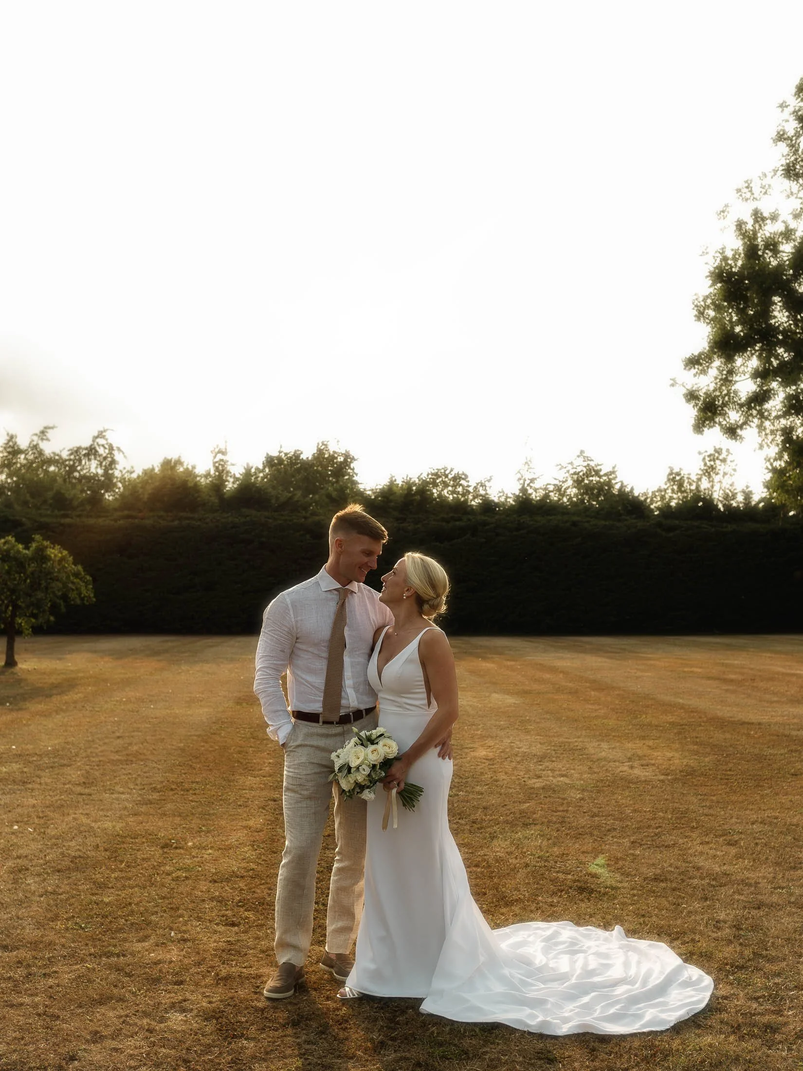 A bride and groom stand together in the grounds of Winters Barns wedding venue as the golden hour sun backlights them.