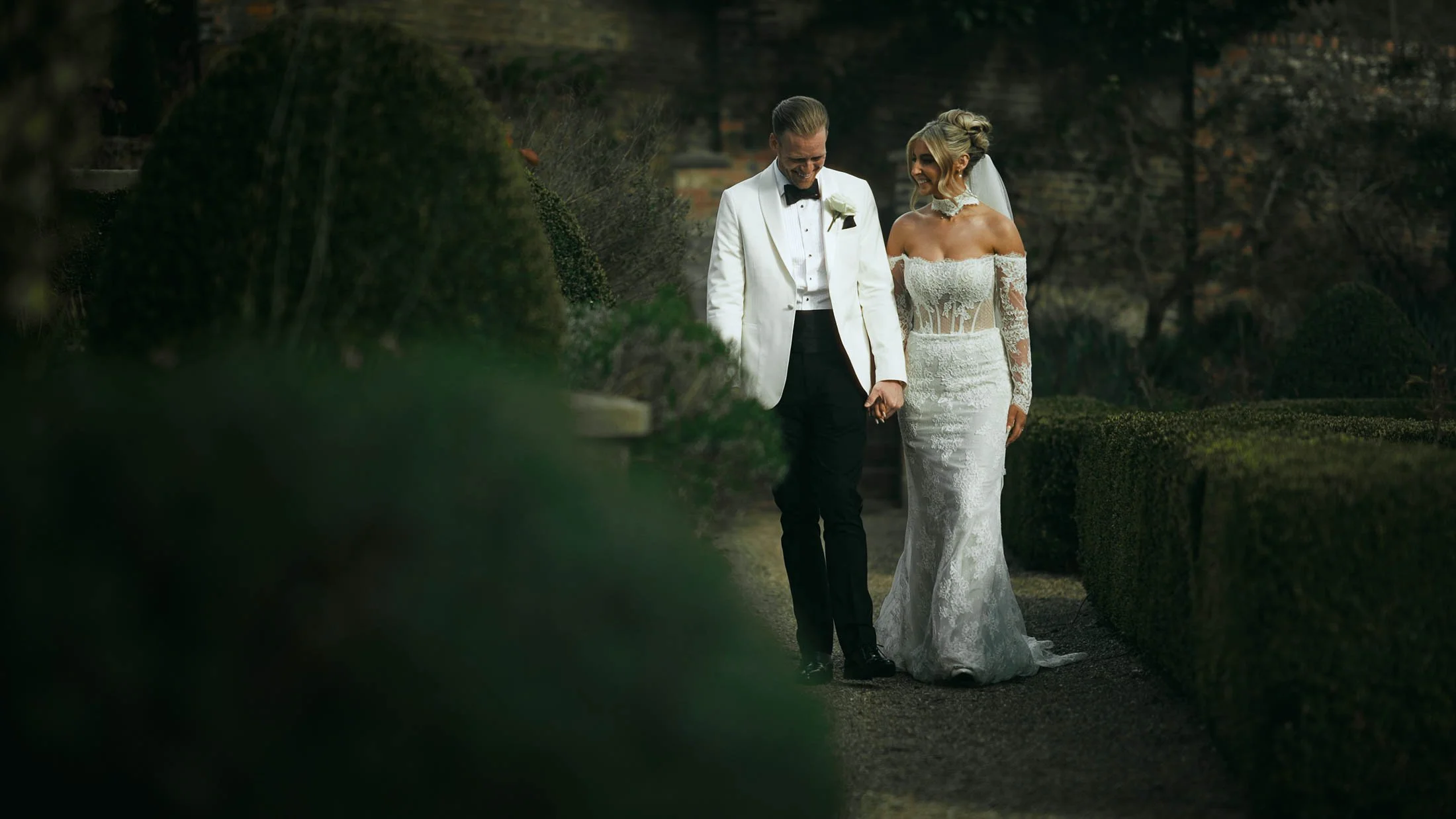 A couple walk holding hands through the grounds of The Orangery, Maidstone, in an intimate moment during a storytelling wedding film.