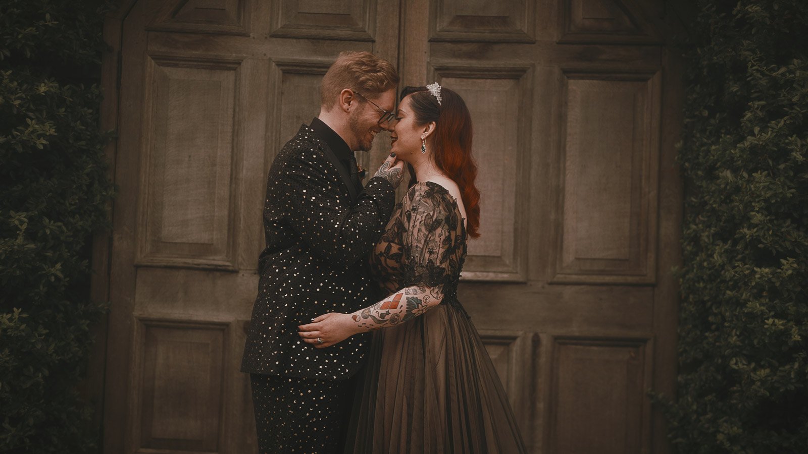 Alternative wedding portrait in front of wooden barn doors framed by greenery