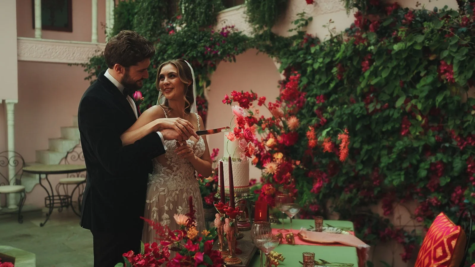 Editorial portrait sequence with black tie styling and saturated colour as the couple cut their wedding cake on a table full of bright pink and red detailing.