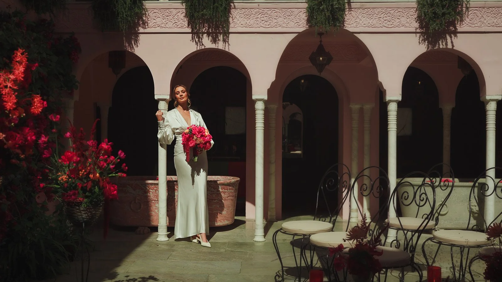 An editorial fashion portrait of a bride surrounded by archways in a courtyard and bright, colourful pink decor and details.