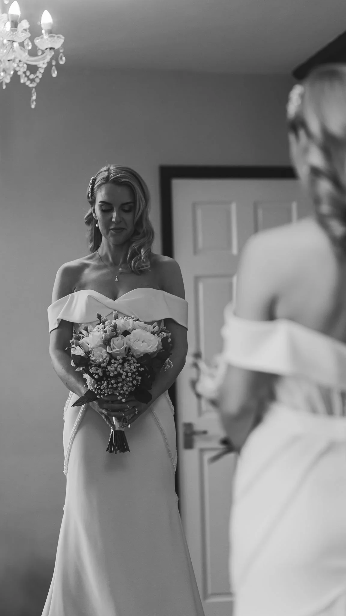 Black and white reflection of a bride holding her bouquet during morning preparations.