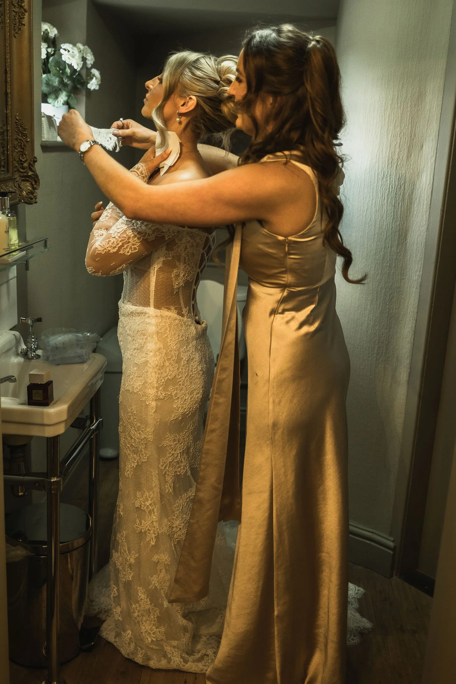 A bridesmaid helps a bride put on her necklace as she gets into her wedding dress at The Orangery Maidstone.