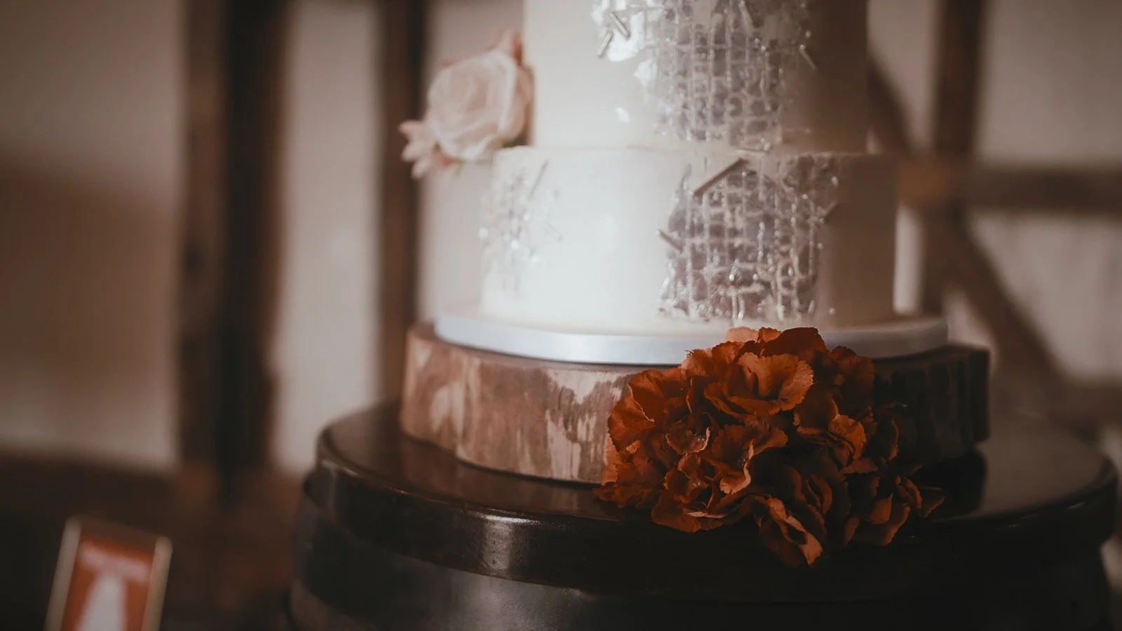 A wedding cake sits on an oak barrel in the entrance hall of a colourful Winters Barns wedding in Kent.