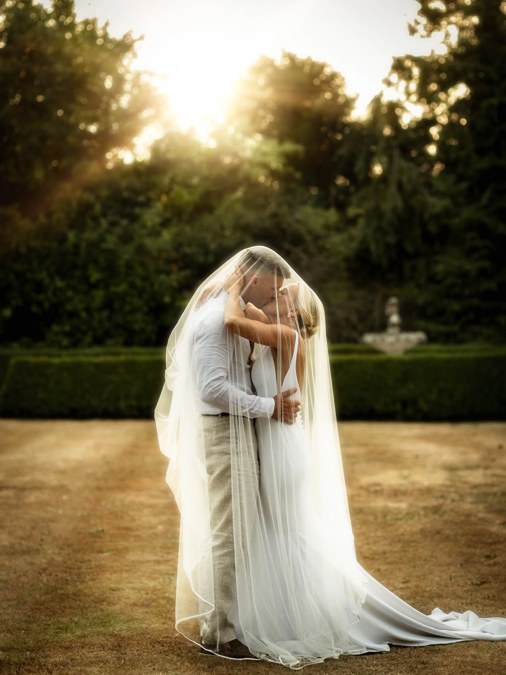 An editorial wedding photograph captured at Winters Barns in Kent, UK, as a bride and groom kiss underneath a veil as the golden hour sunlight illuminates them.
