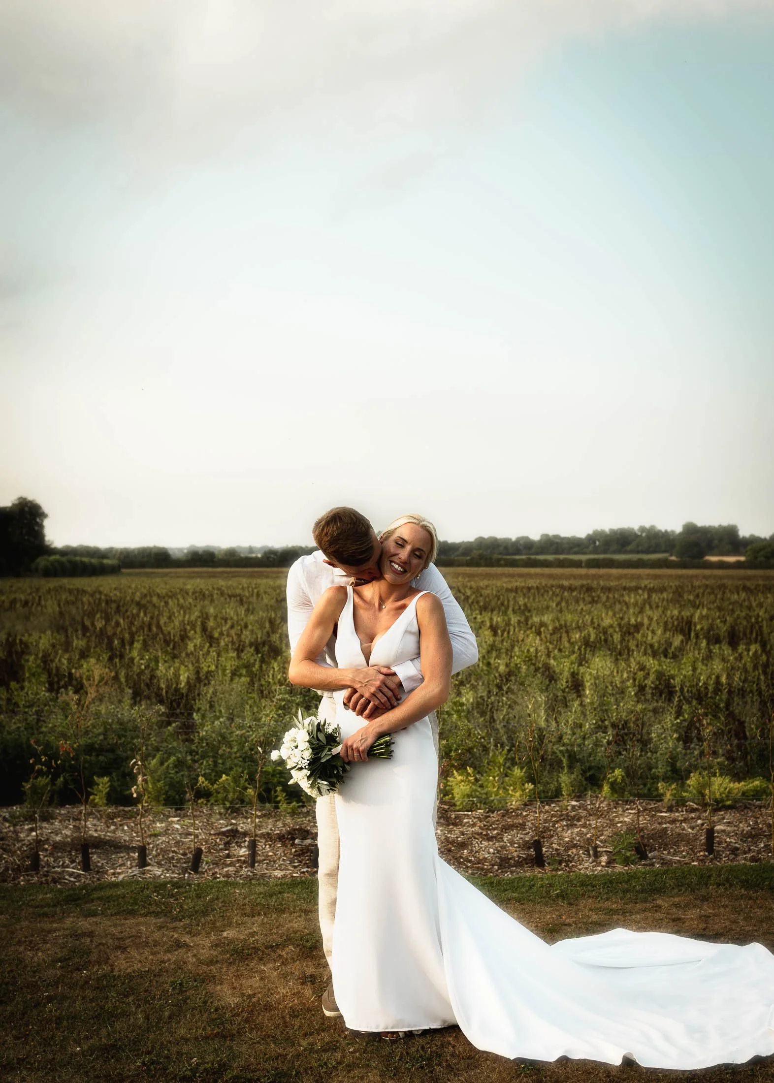 A wide-angle couples wedding portrait of a bride and groom laughing at sunset at Winters Barns, Canterbury, Kent.