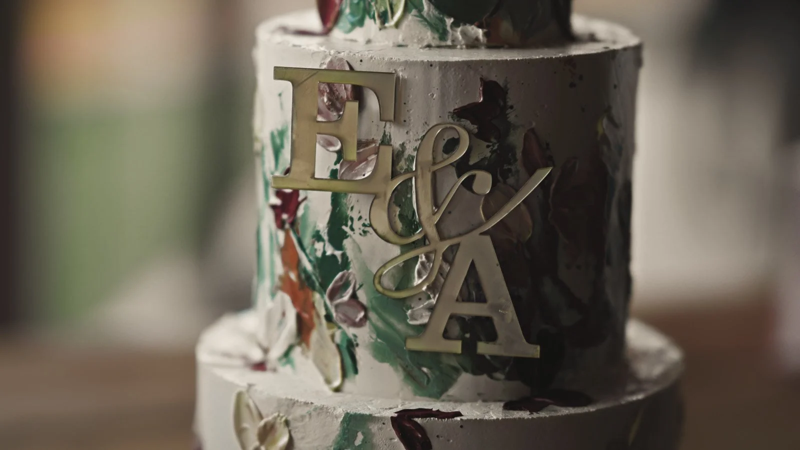 Close-up of a colourful luxury wedding cake with bold red, orange and green florals and the bride and grooms initials written in gold lettering  at a riverside wedding on the Thames.