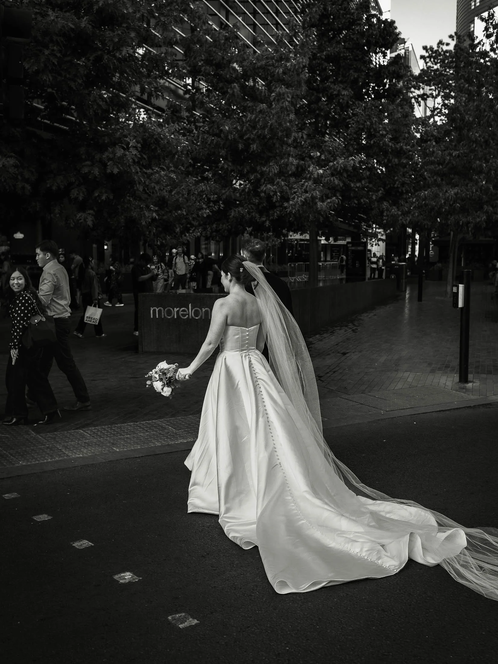 A timeless and classic London wedding photograph showing a bride and groom crossing a busy street in a black and white aesthetic.