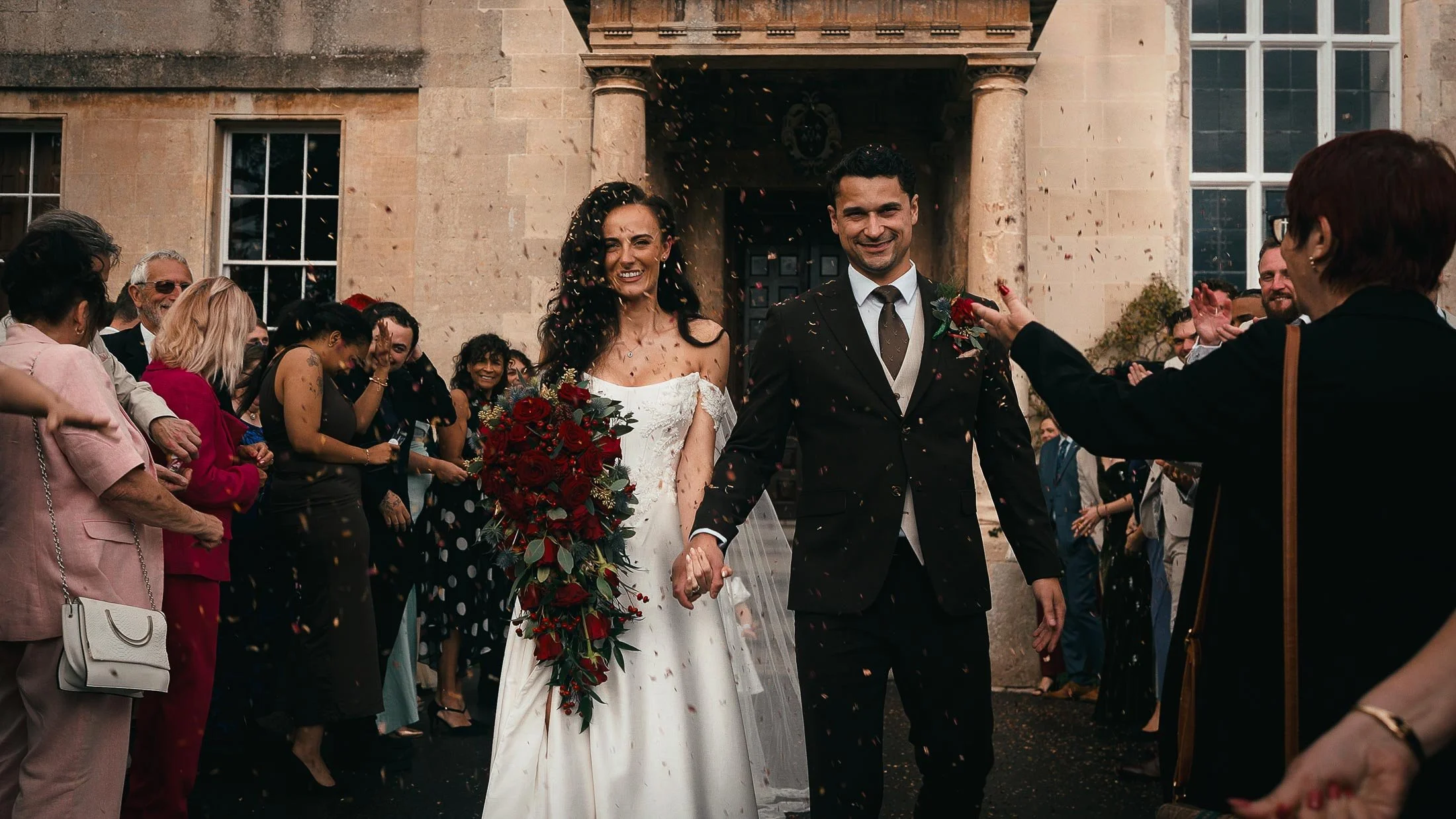 Bride and groom exit their wedding ceremony at Elmore Court as guests throw confetti.
