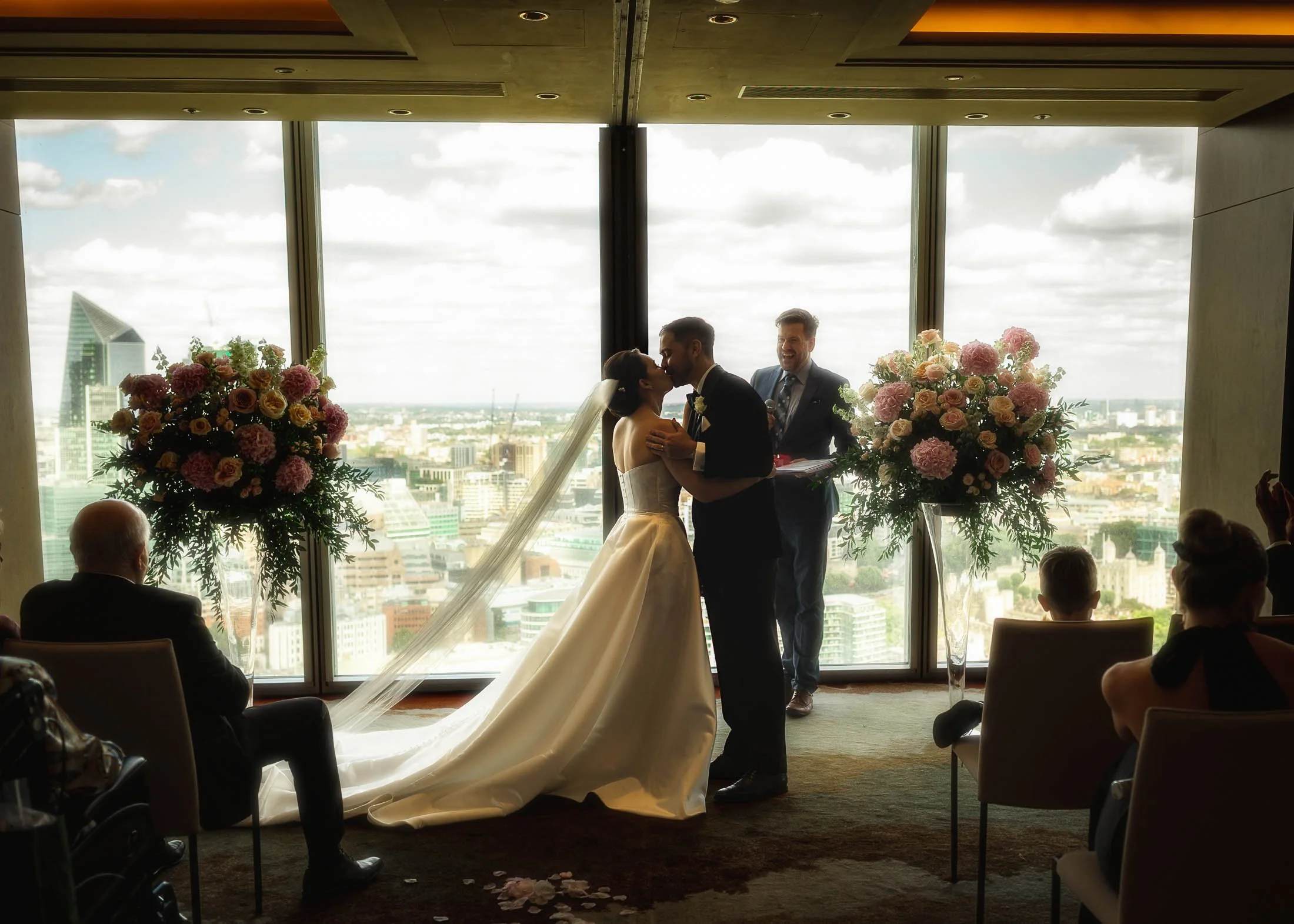 A wide shot of a bride and grooms first kiss during their indoor London wedding ceremony at the Shangri-La hotel in The Shard.