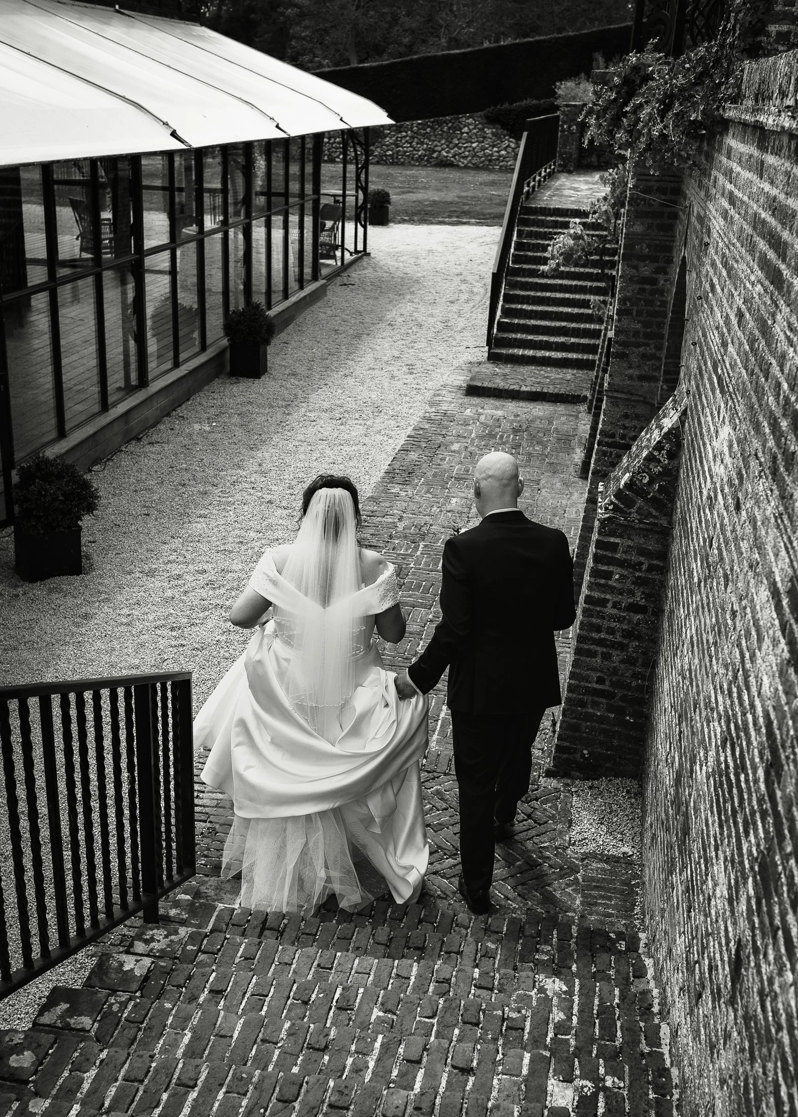An editorial portrait of Lucy & Luke walking towards the Gass Orangery at Port Lympne on their wedding day.