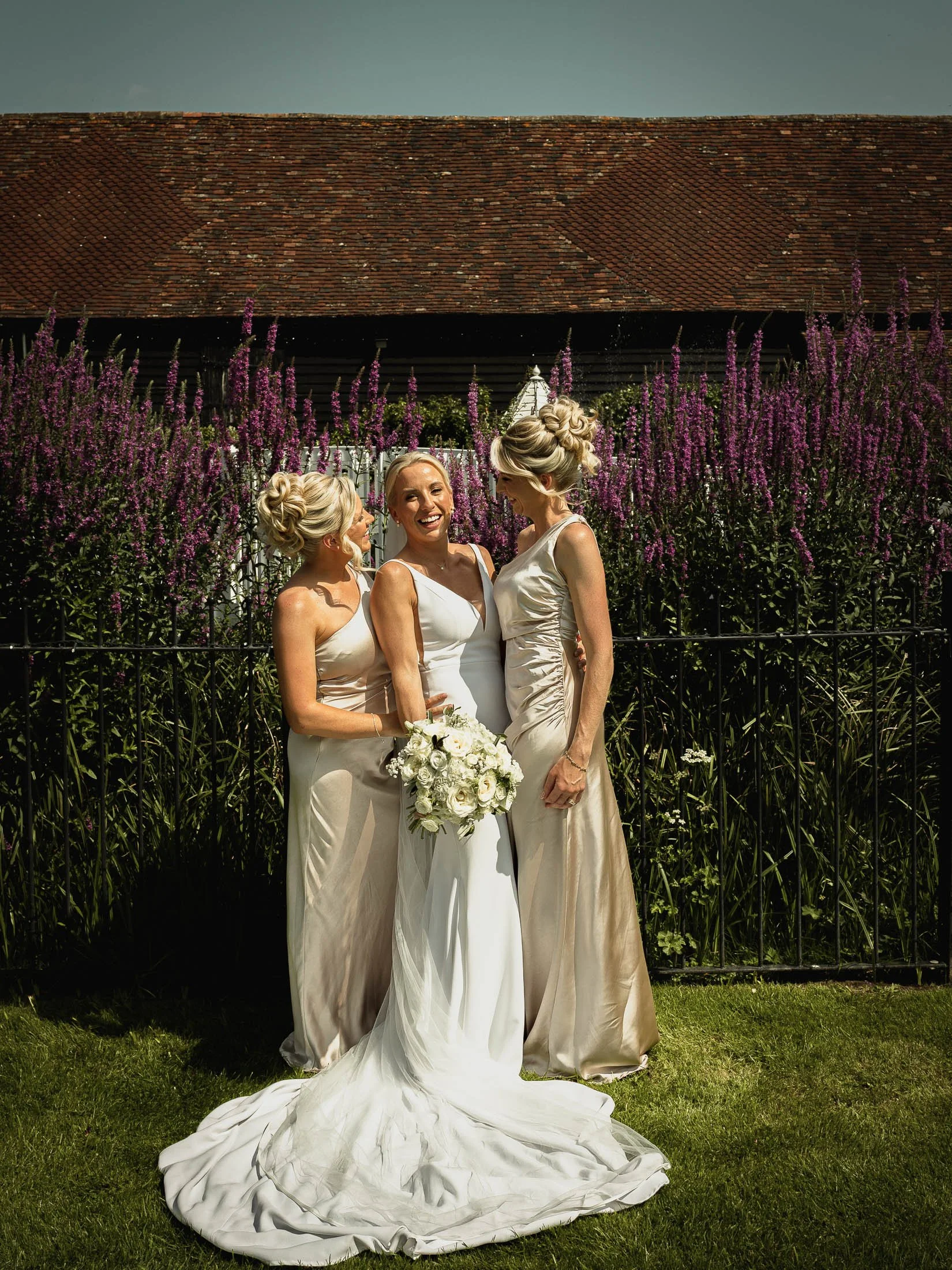 A relaxed group photo of a bride with her sisters and bridesmaids during a summer outdoor wedding reception at Winters Barns in Kent.