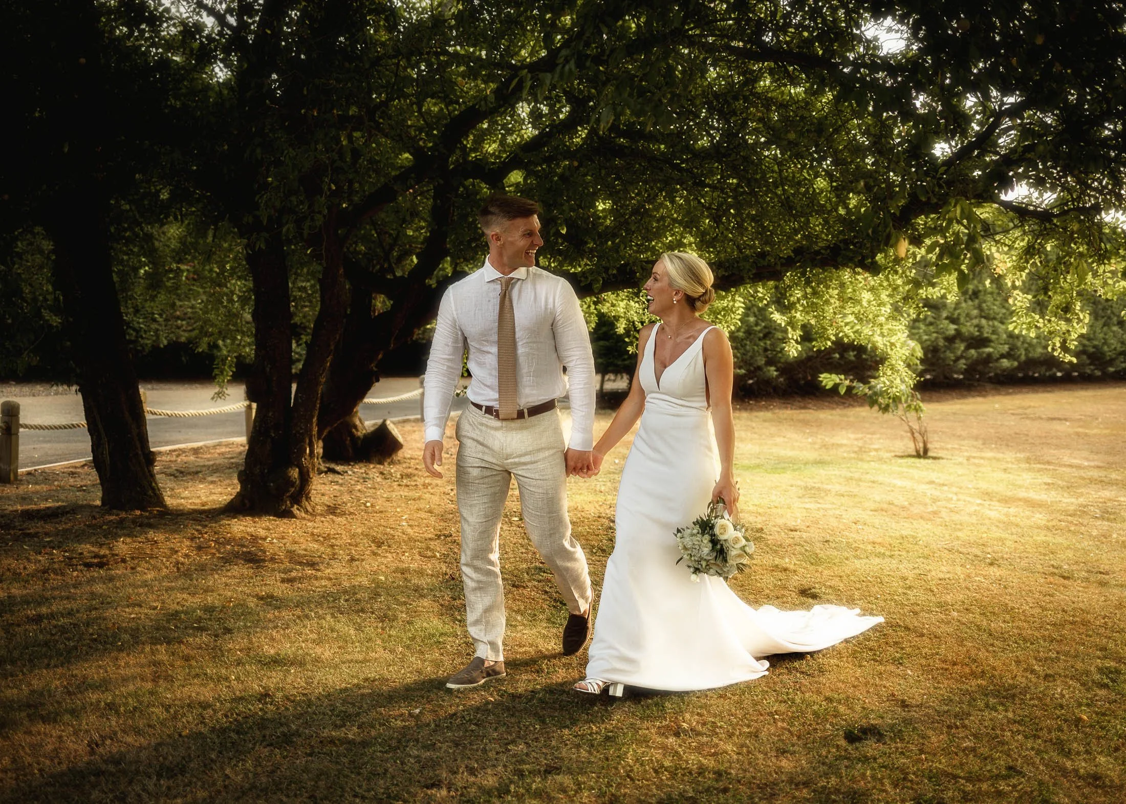 A dreamy wedding photograph as a bride and groom hold hands and walk through woodland at golden hour during their Kent wedding at Winters Barns.