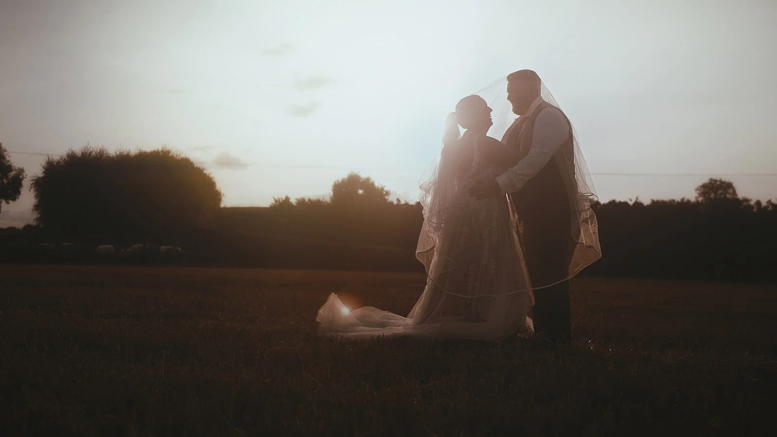 Romantic wide shot of the couple in open fields near Winters Barns for a cinematic wedding film frame.