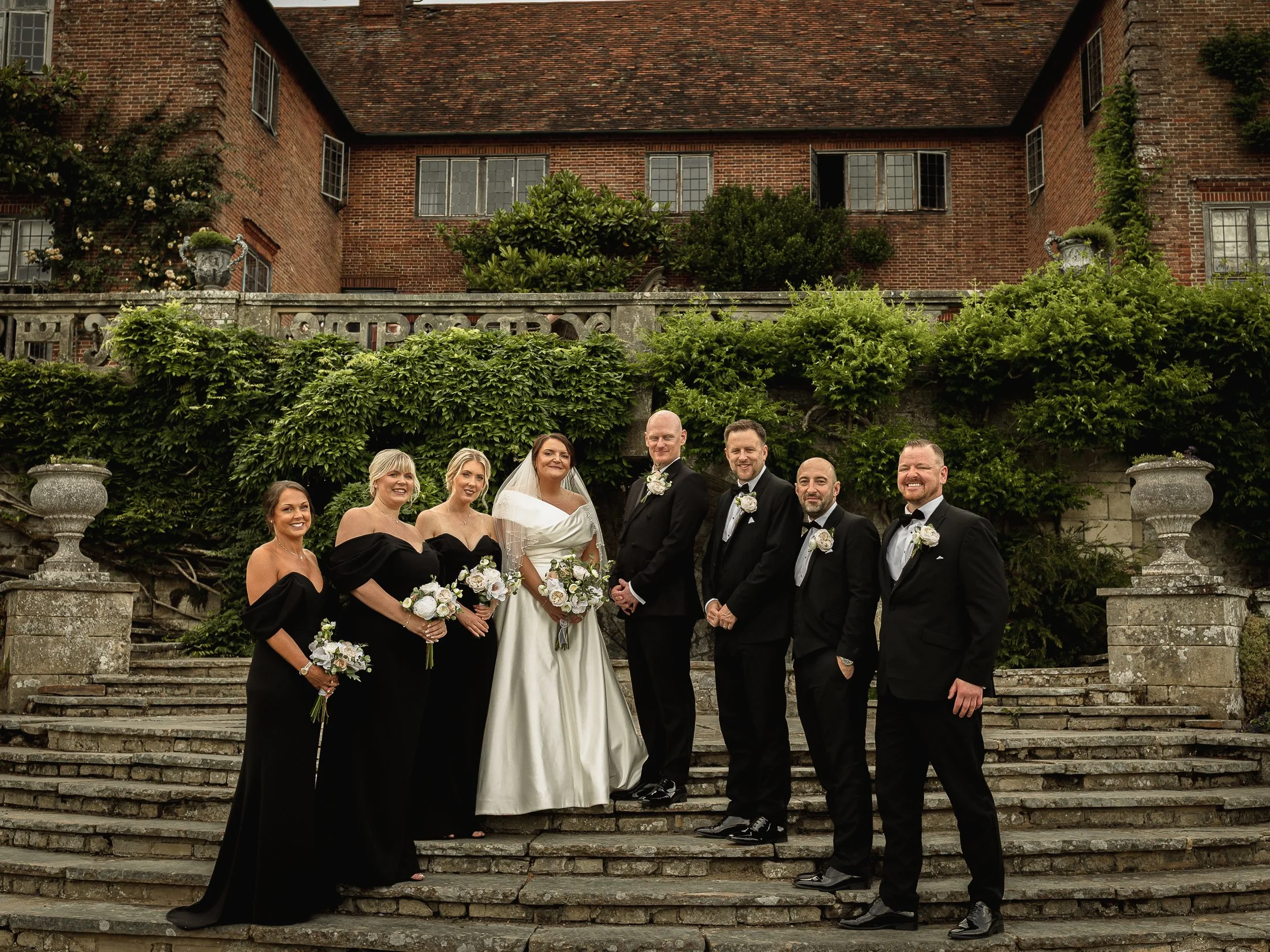 A bridal party in black tie aesthetic stand on the mansion steps at Port Lympne Hotel & Reserve wedding.
