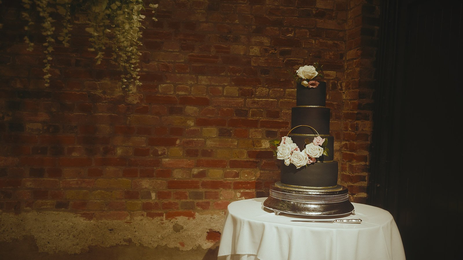Editorial shot from a wedding film of a four tier navy blue wedding cake in the Tithe Barn at Cooling Castle Barn, Kent.