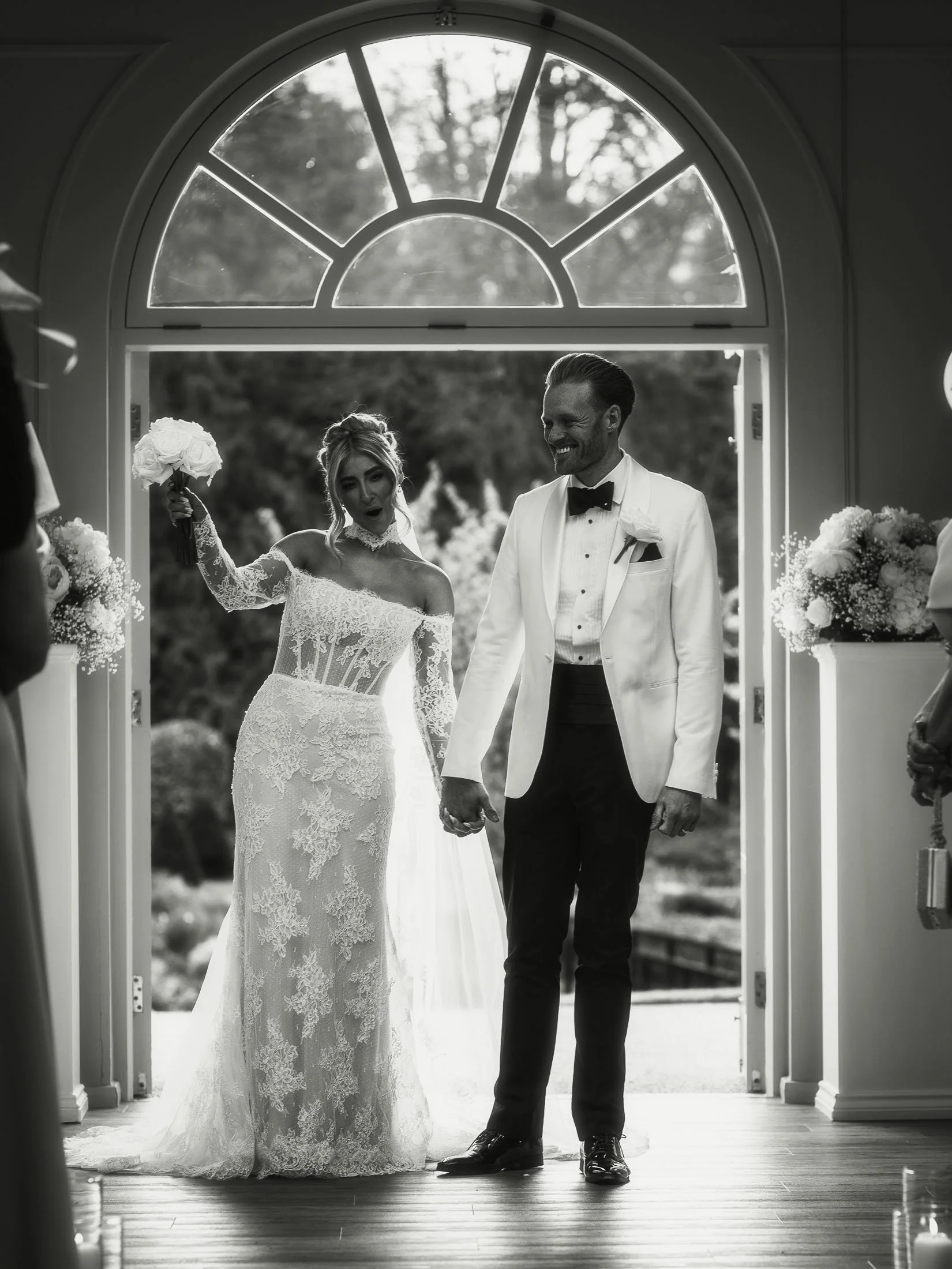 A black and white editorial style wedding photograph of a bride and groom celebrating at the end of an indoor wedding ceremony.