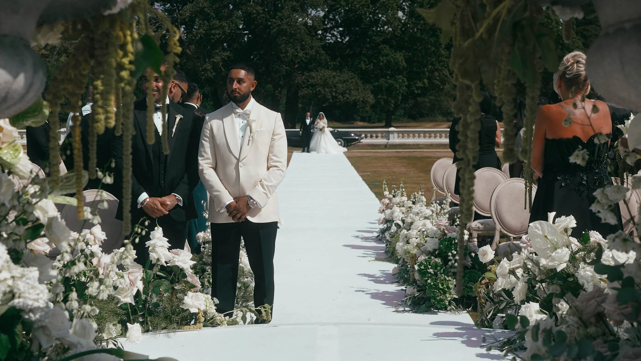 A groom in black tie waits at the end of the aisle during his outdoor wedding ceremony at Grantley Hall.